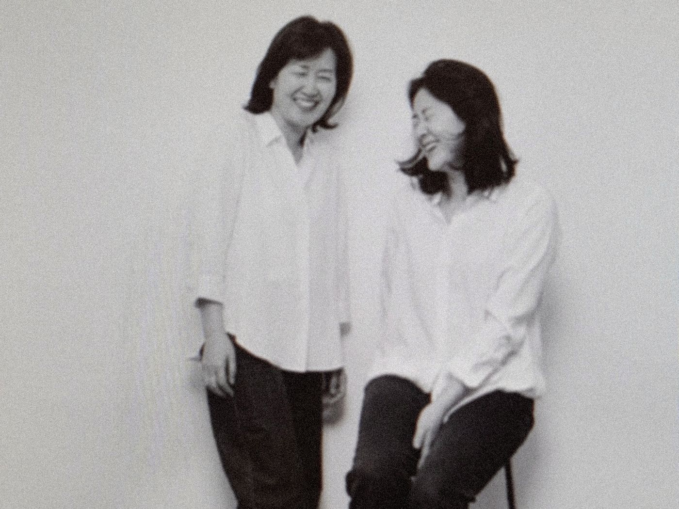 Miye and Min laughing together against a white wall, both in white shirts