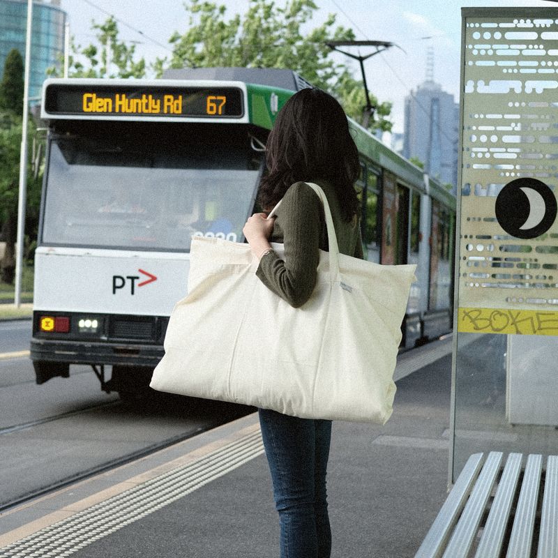 A woman at a Melbourne tram stop with a large Litual bag over her shoulder