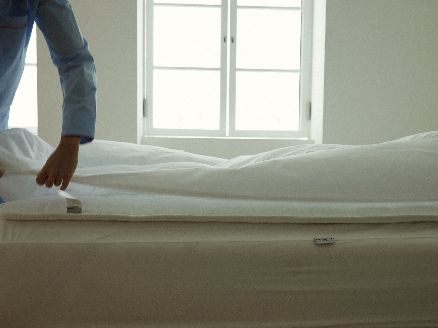 Pulling a fitted sheet over Litual on a bare mattress, in a bright room