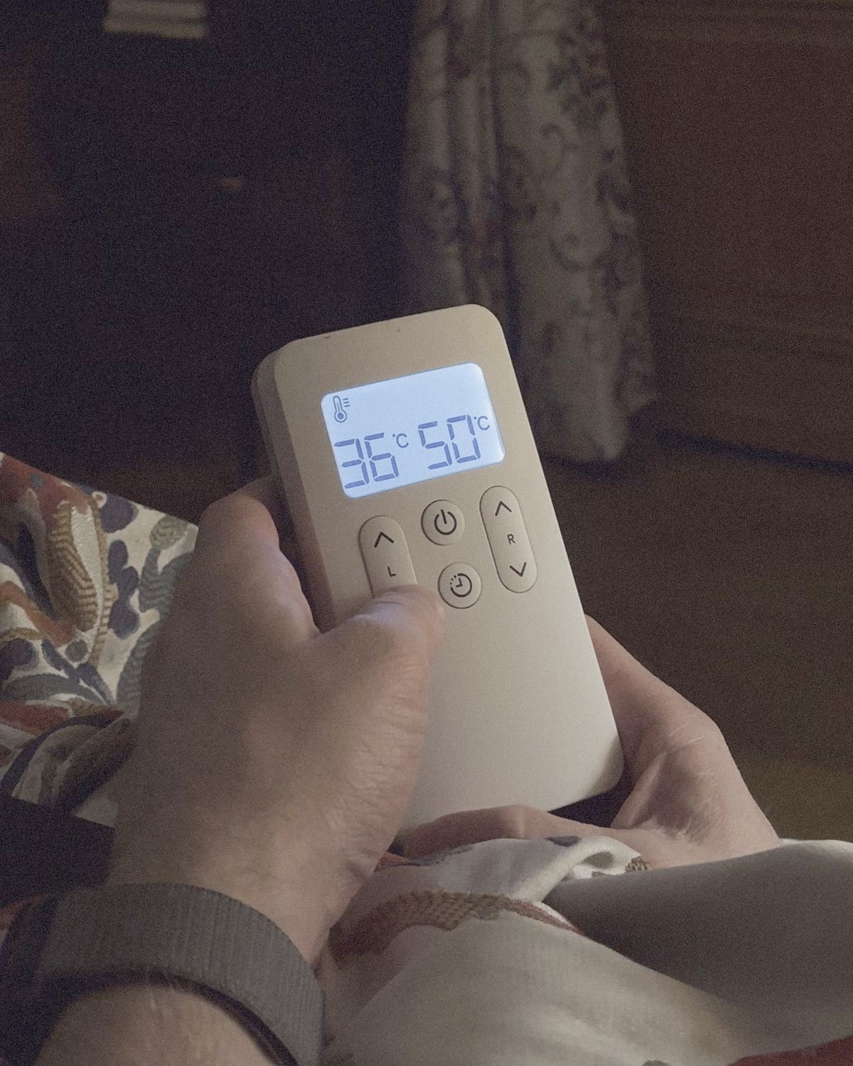 A hand holding the Litual controller in a dark room — the screen reads 36°C for the left side and 50°C for the right