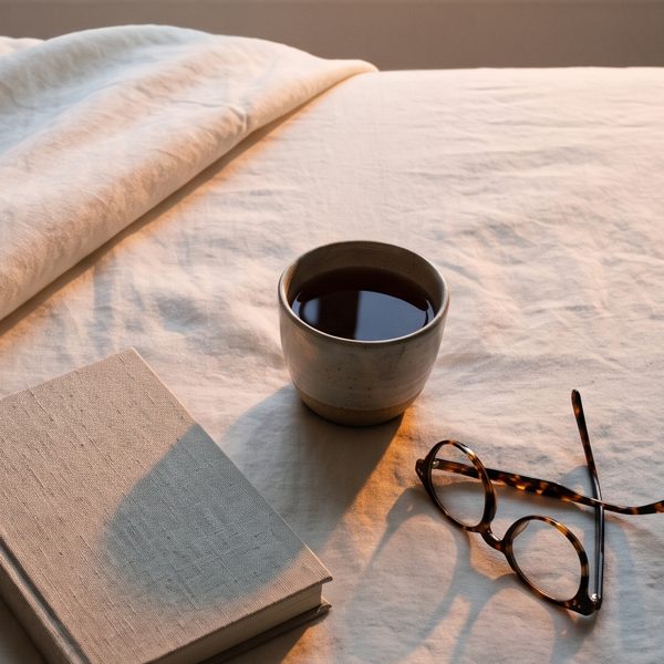 Morning light on the folded-back duvet, a cup of tea on the linen