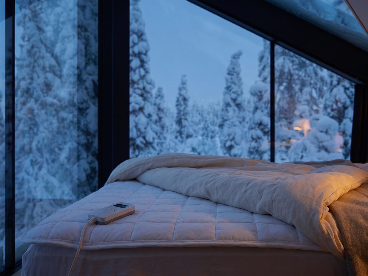 The Litual topper on a bed under an attic window, snow-covered forest outside, one warm lamp inside