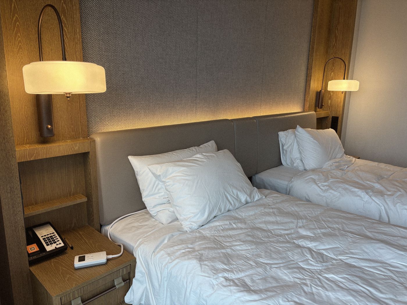 Twin hotel beds under reading lamps, a Litual controller on the bedside table