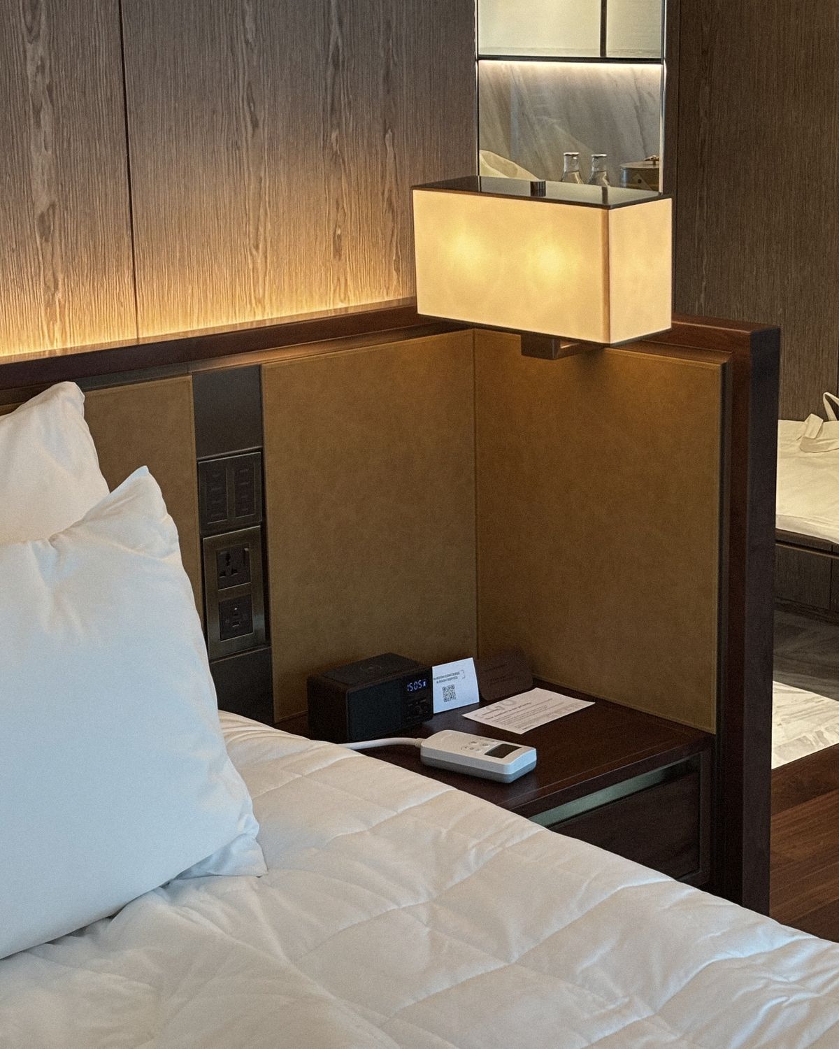 A hotel bedside at night — lamp lit, the Litual controller resting beside the clock