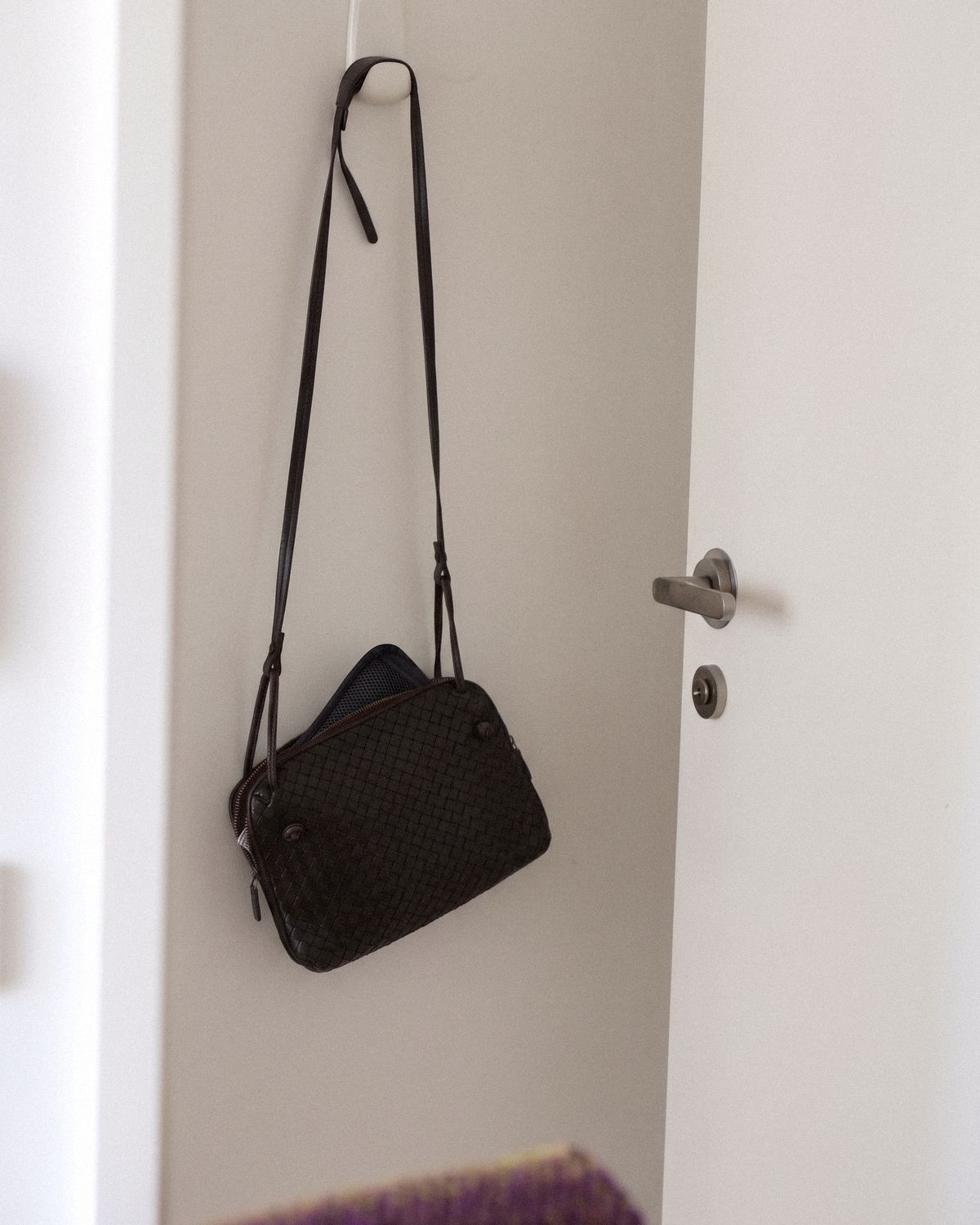 A small woven handbag hanging on a door hook, the mesh pouch of the Poom just showing at the zip