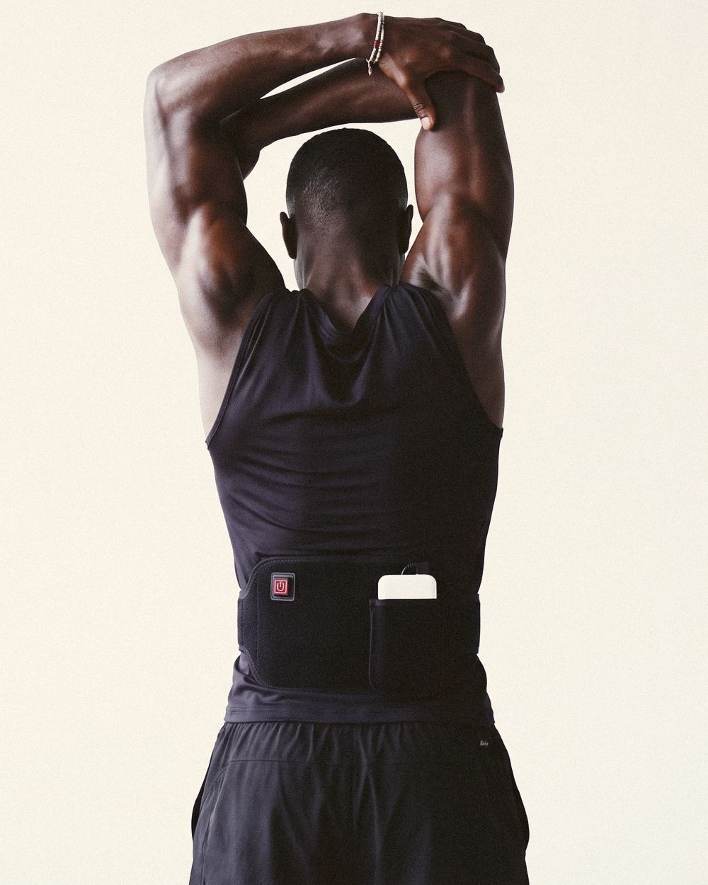 A man stretching with his arms overhead, Poom worn at the lower back